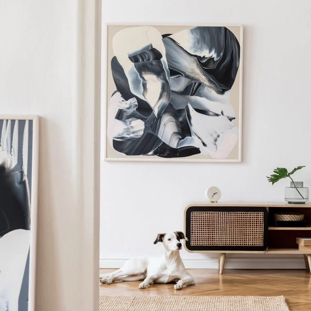 Grande peinture abstraite noire et blanche au-dessus d’un meuble en cannage, un chien couché devant